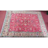 A large Kashan style rug with repeat motifs on a rouge floral back ground surrounded by a stylised