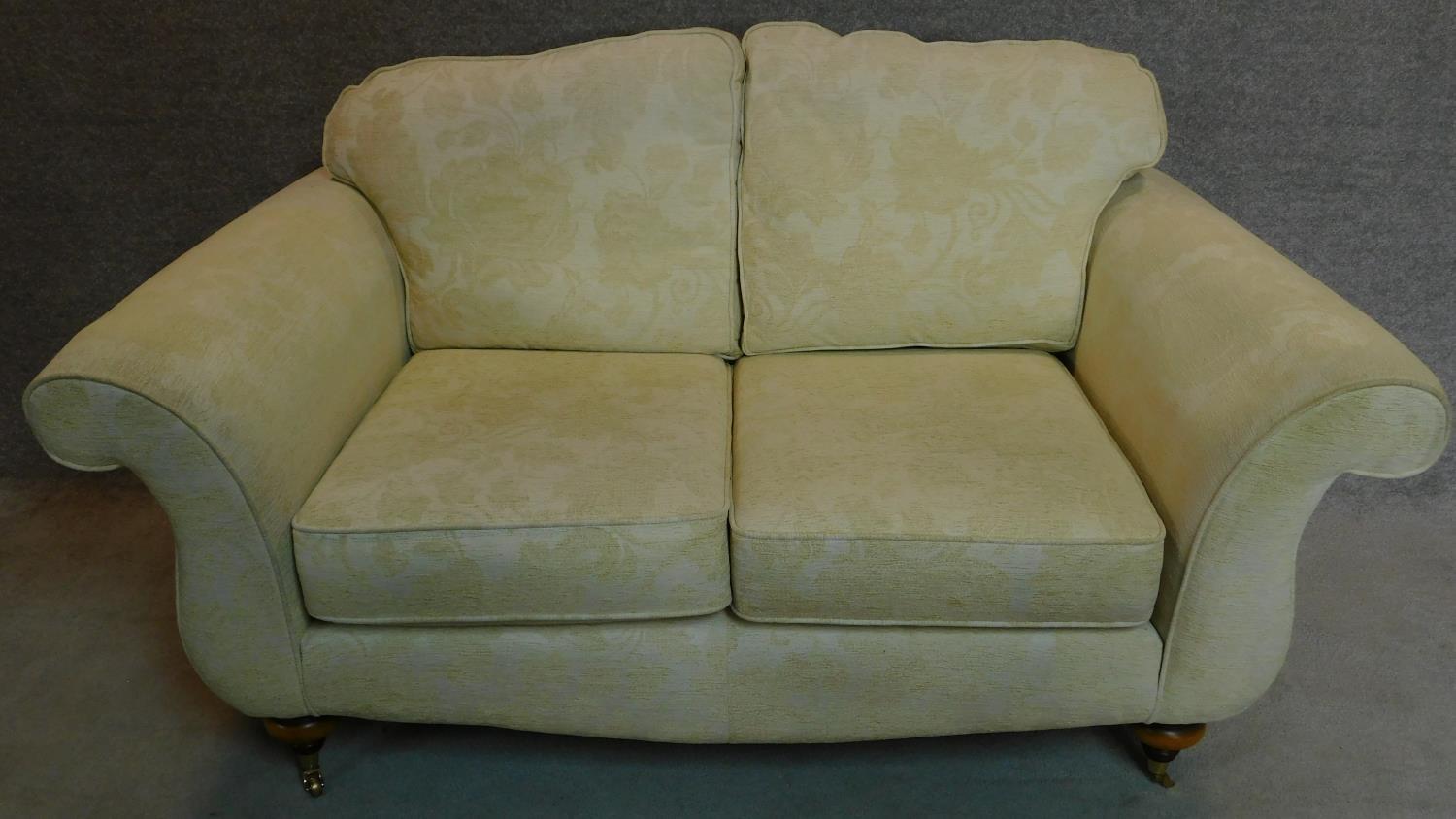 A two seater Victorian style sofa upholstered in beige floral upholstery on turned mahogany feet