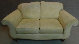 A two seater Victorian style sofa upholstered in beige floral upholstery on turned mahogany feet