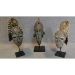 Three carved and painted African tribal masks on stands. H.55 (tallest)