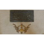 A cast metal relief panel depicting cherubs hunting deer and a classical style ormolu mount.