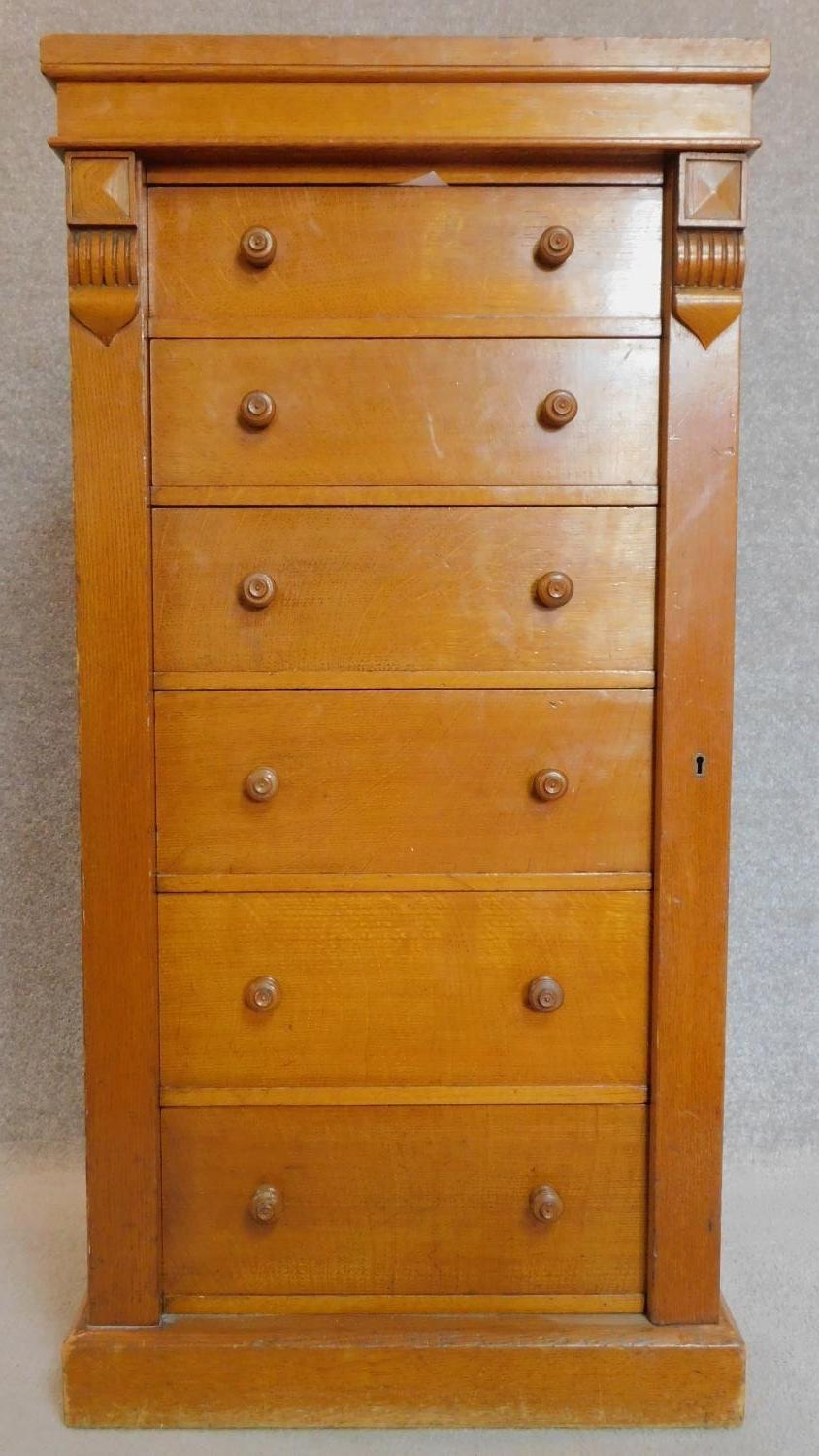 A Victorian honey oak Wellington chest of six oak lined graduating drawers flanked by carved