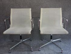 A pair of white mesh and chrome swivel armchairs designed by Charles Eames, Vitra makers label to