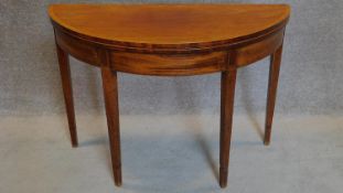 A Georgian mahogany and satinwood strung demi lune foldover top tea table on square tapering