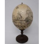 A scrimshaw ostrich egg on bronze stand, engraved with whales and sailing ship scene, map and