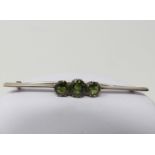 A three stone green sapphire and white metal bar brooch, set with three cushion shaped old cut green