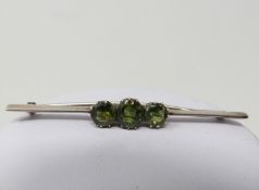 A three stone green sapphire and white metal bar brooch, set with three cushion shaped old cut green