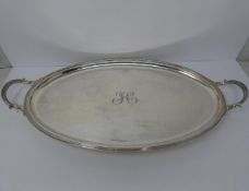 A large silver oval tray, monogrammed with H, round pebble feet, foliate design handles, ridged rim,