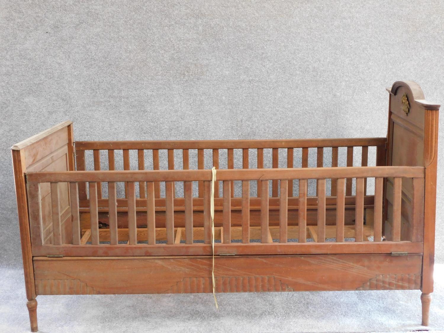 An early 20th century walnut child's bed with satinwood and ebony stringing and floral marquetry
