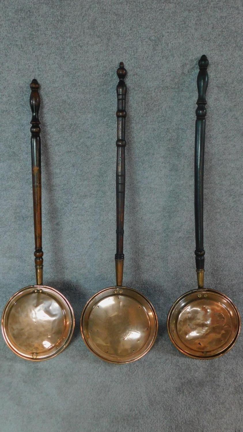 A collection of three 19th century copper warming pans with turned handles. W.116cm.