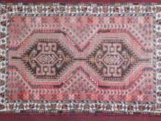 A Persian rug with two diamond medallions on a rouge ground, within geometric border, 155x111cm