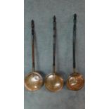 A collection of three 19th century copper warming pans with turned handles. W.116cm.