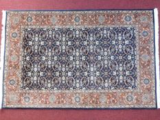 A Persian rug with repeating petal motifs on a sapphire field surrounded by a rouged floral border