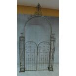 A metal garden arch with a pair of decorative arched gates flanked by wrought pilasters H.254cm W.