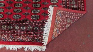 A large Bokhara carpet, repeating meddallions on burgundy ground within multi-border. L.301cm W.