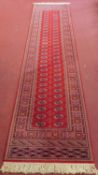 A Bokhara runner on a rouge field surrounded by geometric border with fringes. 364x85cm