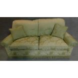 A two seater sofa in floral green upholstery. 77x188x85cm