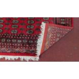 A large handmade woollen Bokhara rug with repeating medallions on a burgundy ground within multi-