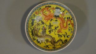 A Chinese yellow ground ceramic dish depicting two dragons, one red and one black. Greek key pattern