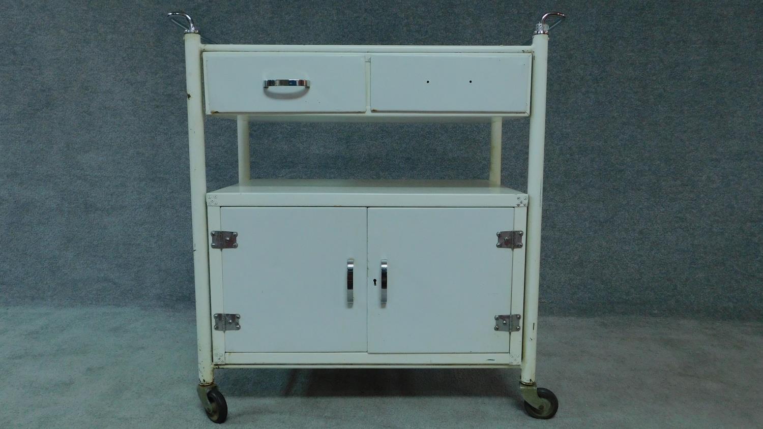 A white painted and metal medical cabinet/trolley with drawers and cupboards on casters. H.90 W.86