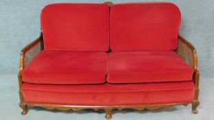 A mid 20th century walnut framed bergere sofa with caned panelled back and sides in red upholstery