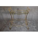 A brass framed oval glass topped drinks trolley on casters. 85cm wide x 85cm high.