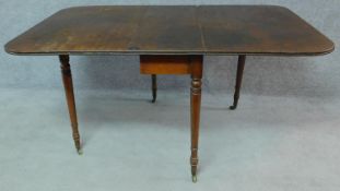 A Regency mahogany drop flap dining table on turned tapering supports terminating in brass cup