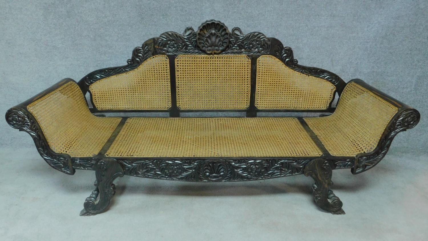 A Colonial style carved hardwood scroll end sofa with caned back and sides on scroll supports. H.101