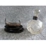 A silver collared cut glass perfume bottle and a silver wire boat on wooden stand. Perfume bottle