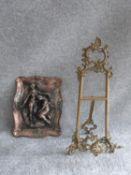 A copper relief moulded wall plaque with male and female figures and a vintage brass openwork easel.