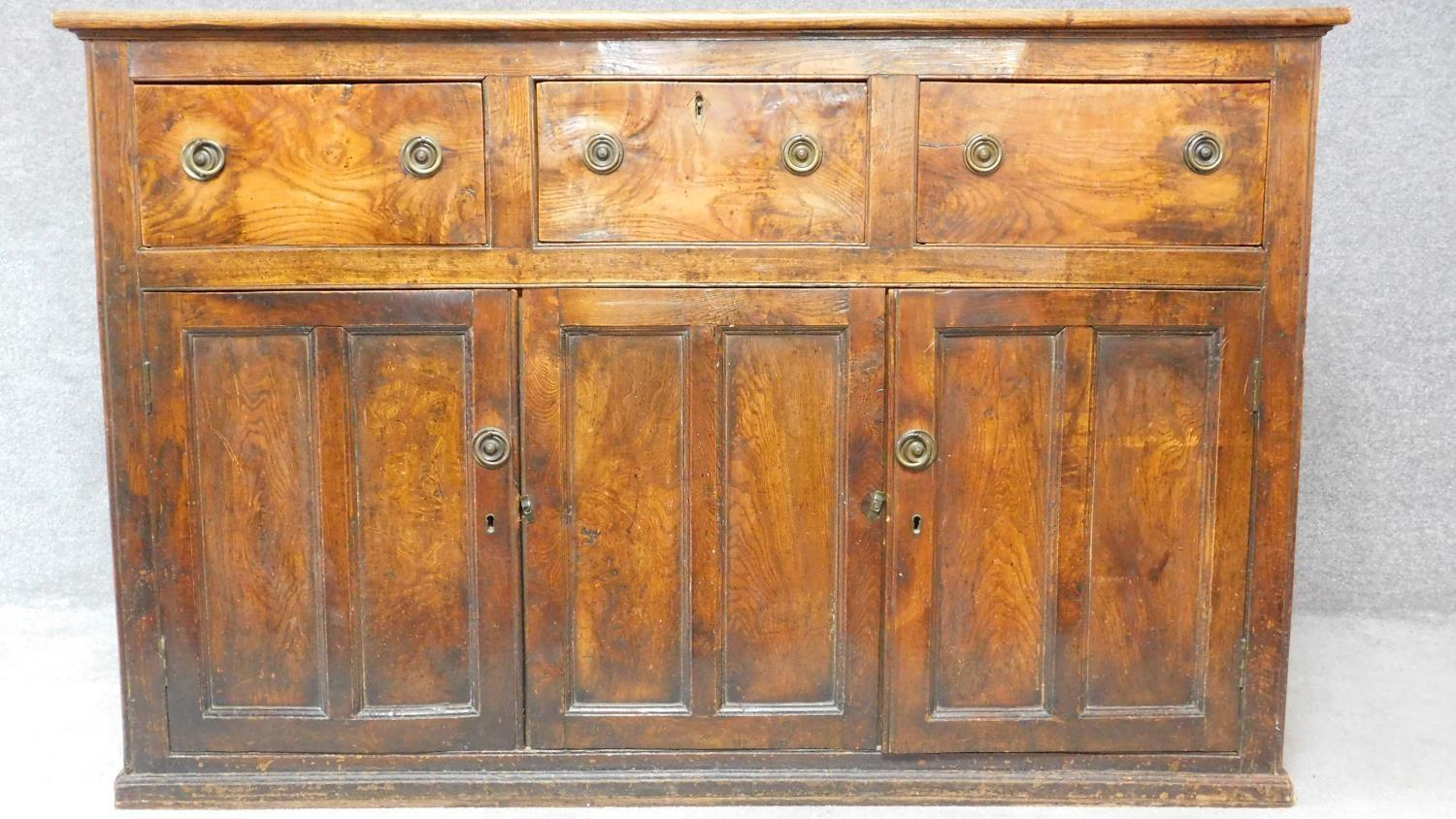 An antique country figured and burr elm dresser base fitted three frieze drawers above panel