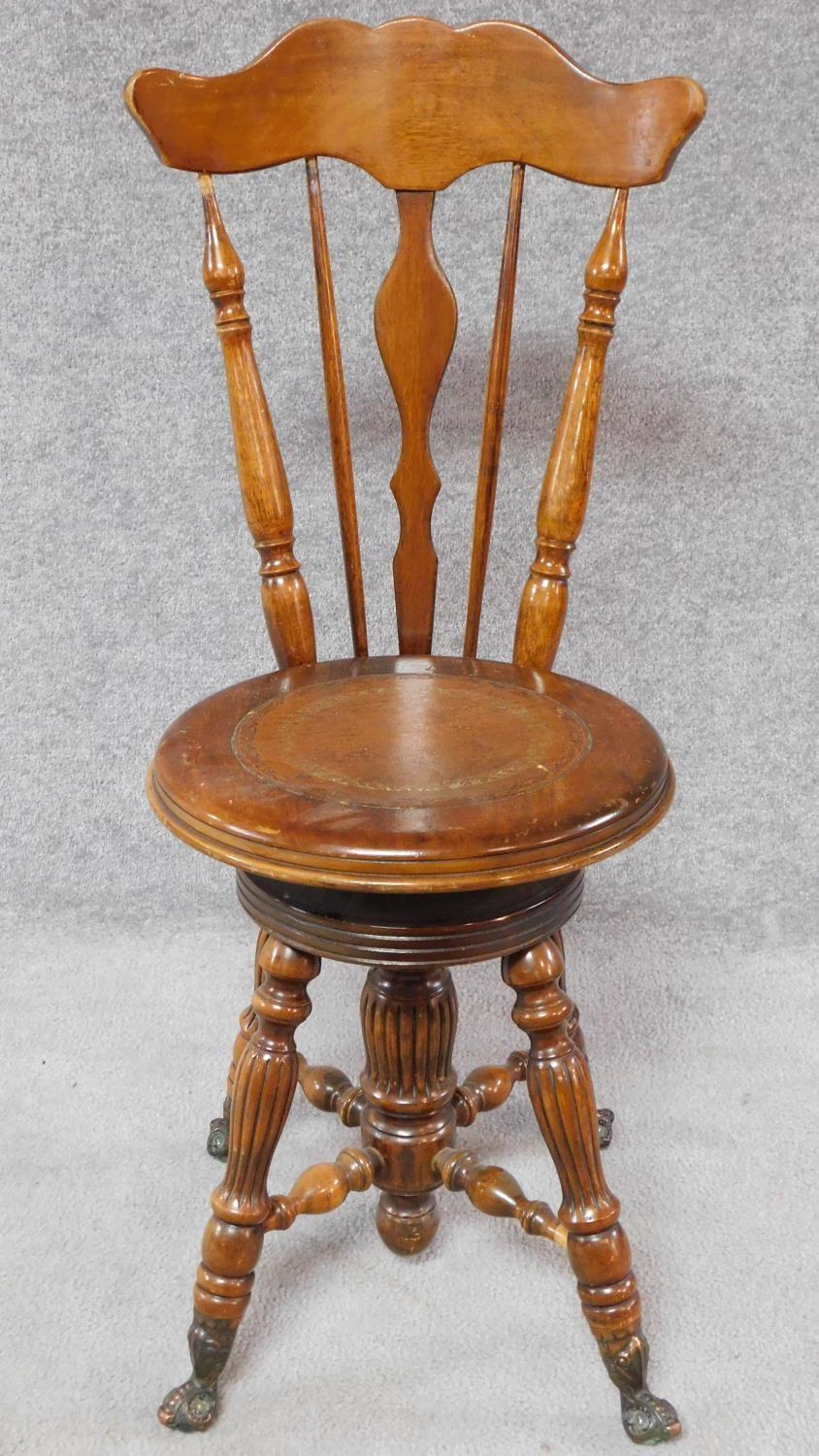 A Victorian walnut revolving piano stool with foliate carving to the back on reeded stretchered