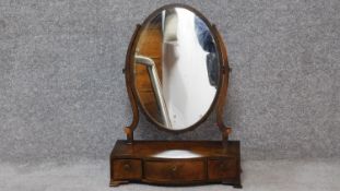 A Georgian mahogany serpentine fronted toilet mirror with oval swing plate on base fitted with