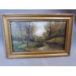 A gilt framed 19th century oil on canvas of a couple sitting under trees by a river. Indistinctly