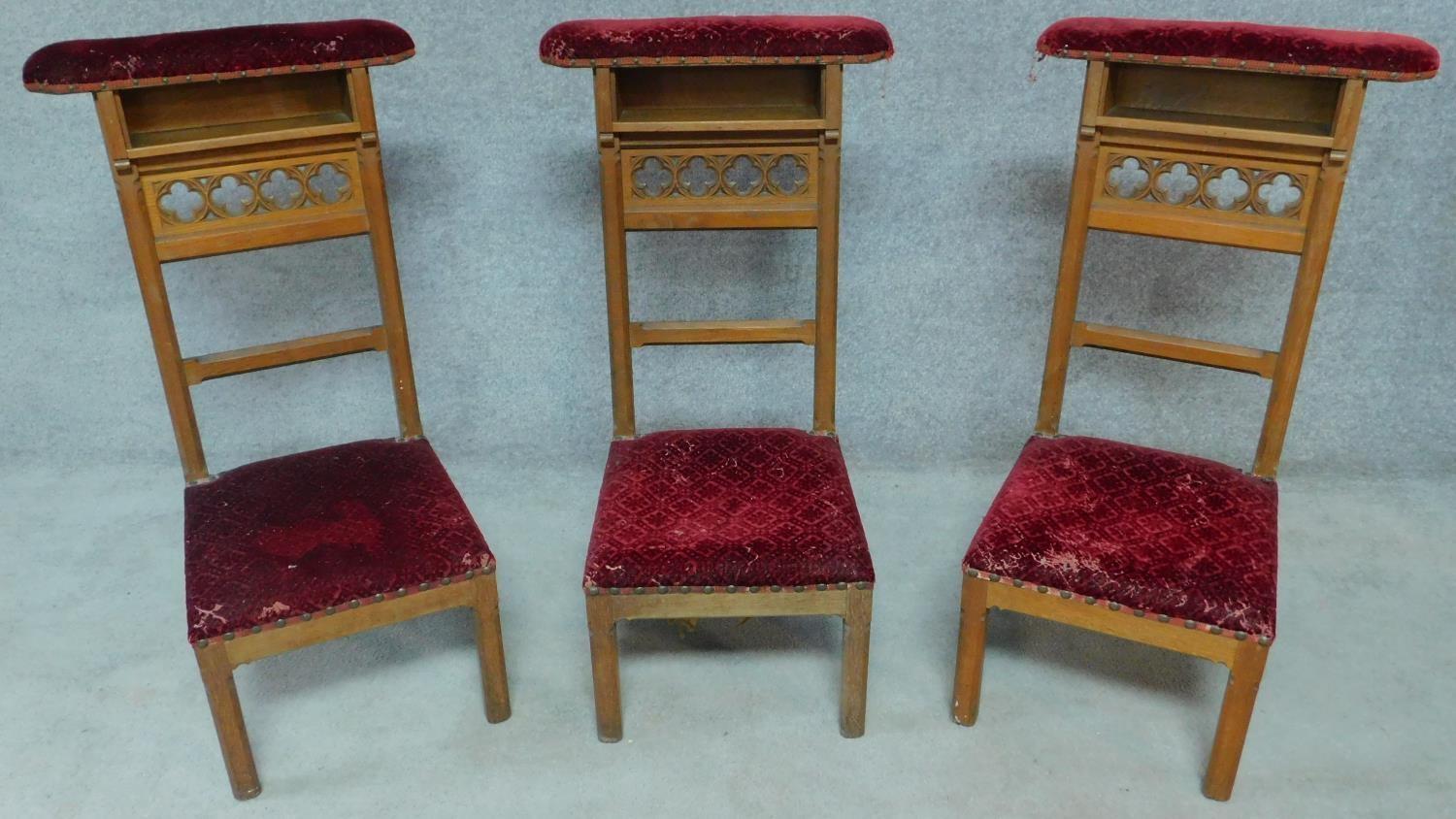 Three late 19th century Gothic style oak prie dieu chairs in burgundy velour upholstery. H.95cm