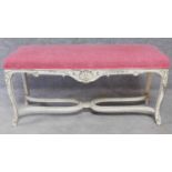 A French Rococo style duet stool with rouge stuffover seat and allover shell and leaf carving on