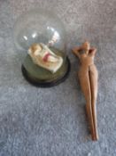 A wax model of a female figure on a chaise longue in an antique glass dome and a wooden nut