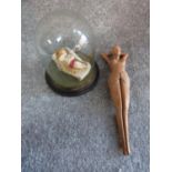 A wax model of a female figure on a chaise longue in an antique glass dome and a wooden nut