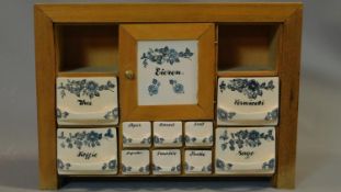 A vintage Dutch herb and spice cabinet with ceramic drawers and door and wooden frame. Central