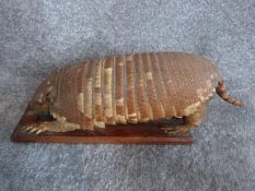 A stuffed armadillo on a wooden base. L 43cm.