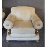 A pair of armchairs in cream fabric with gold detailing and inset gilt metal griffins supporting the