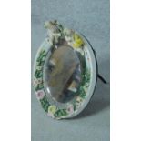 A 19th century porcelain framed German oval bevelled mirror with floral and cherub decoration, by
