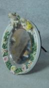 A 19th century porcelain framed German oval bevelled mirror with floral and cherub decoration, by