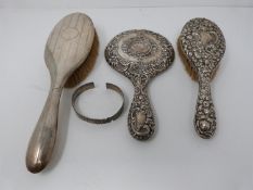 A three piece silver brush and mirror set and a white metal bangle, one brush with engine turned