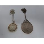 Two silver coins in silver and white metal mounts on silver chains, an American one dollar coin,
