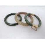 Three round carved jade bangles, one with yellow metal push clasp and safety chain. Largest 9cm