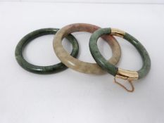 Three round carved jade bangles, one with yellow metal push clasp and safety chain. Largest 9cm