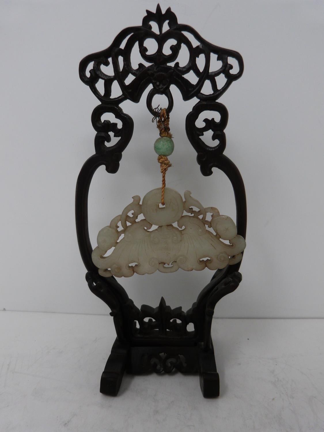 An early 20th century jade pendant on carved wooden stand. Pale celadon jade pendant in the form