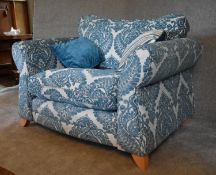 A large armchair with blue patterned fabric upholstery and two scatter cushions. H. 94 x 120 x 94cm