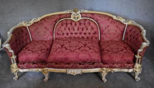 A large gilt and painted framed Rococo style three seater sofa, upholstered in burgundy damask